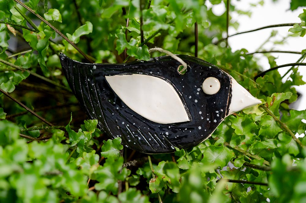 Ceramiczny, czarny kanarek - zawieszka, sfotografowany na tle paproci. Carbonarek.
