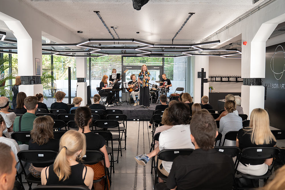 Zdjęcie przedstawia młodych muzyków na scenie w holu Carbonarium. Zdjęcie wykonane zza publiczności siedzącej na krzesełkach.