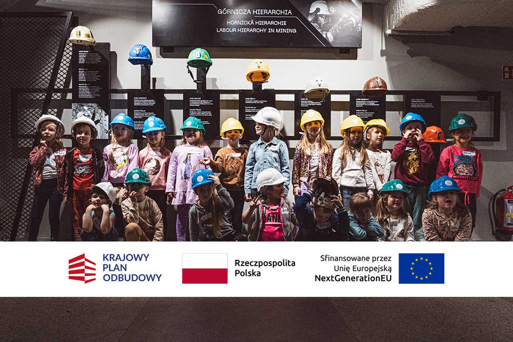 Zdjęcie dzieci z belką z logo KPO, flagą Rzeczypospolitej Polskiej i flagą UE.